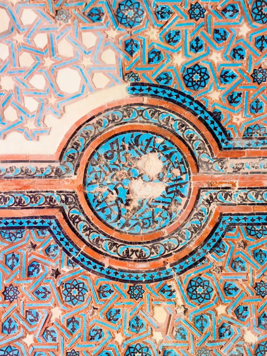 Turkuaz, lacivert ve kiremit renkli geometrik yıldız desenli tarihî çini duvar, ortada yazılı bir madalyon