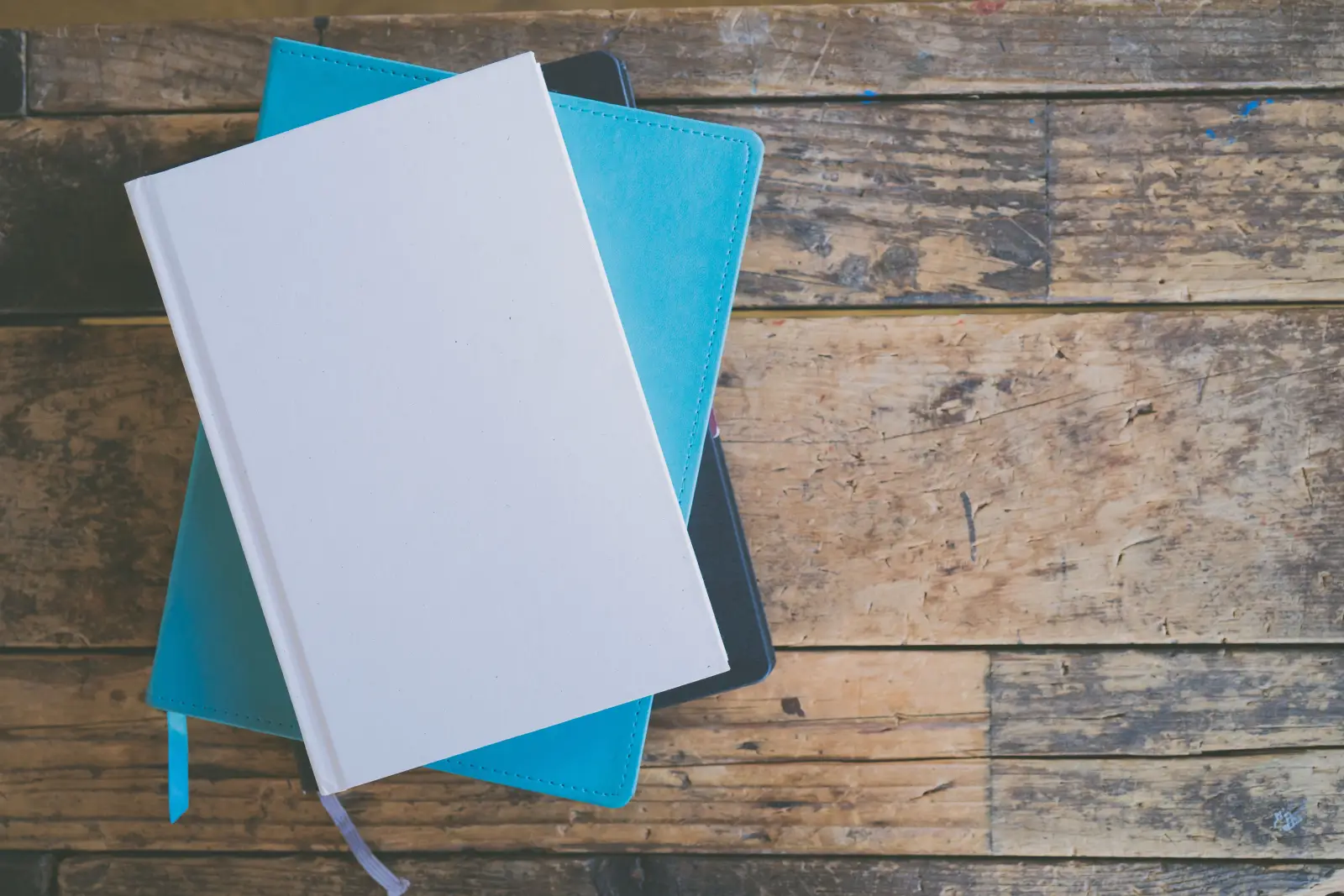Eskimiş ahşap masa üzerinde üst üste duran beyaz ve turkuaz iki defter