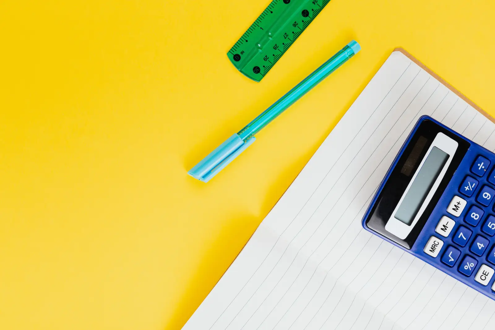Sarı zemin üzerinde çizgili defter, hesap makinesi, kalem ve cetvel