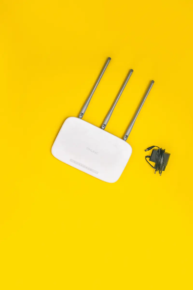 Sarı zemin üzerinde üç antenli beyaz bir kablosuz modem ve adaptörü