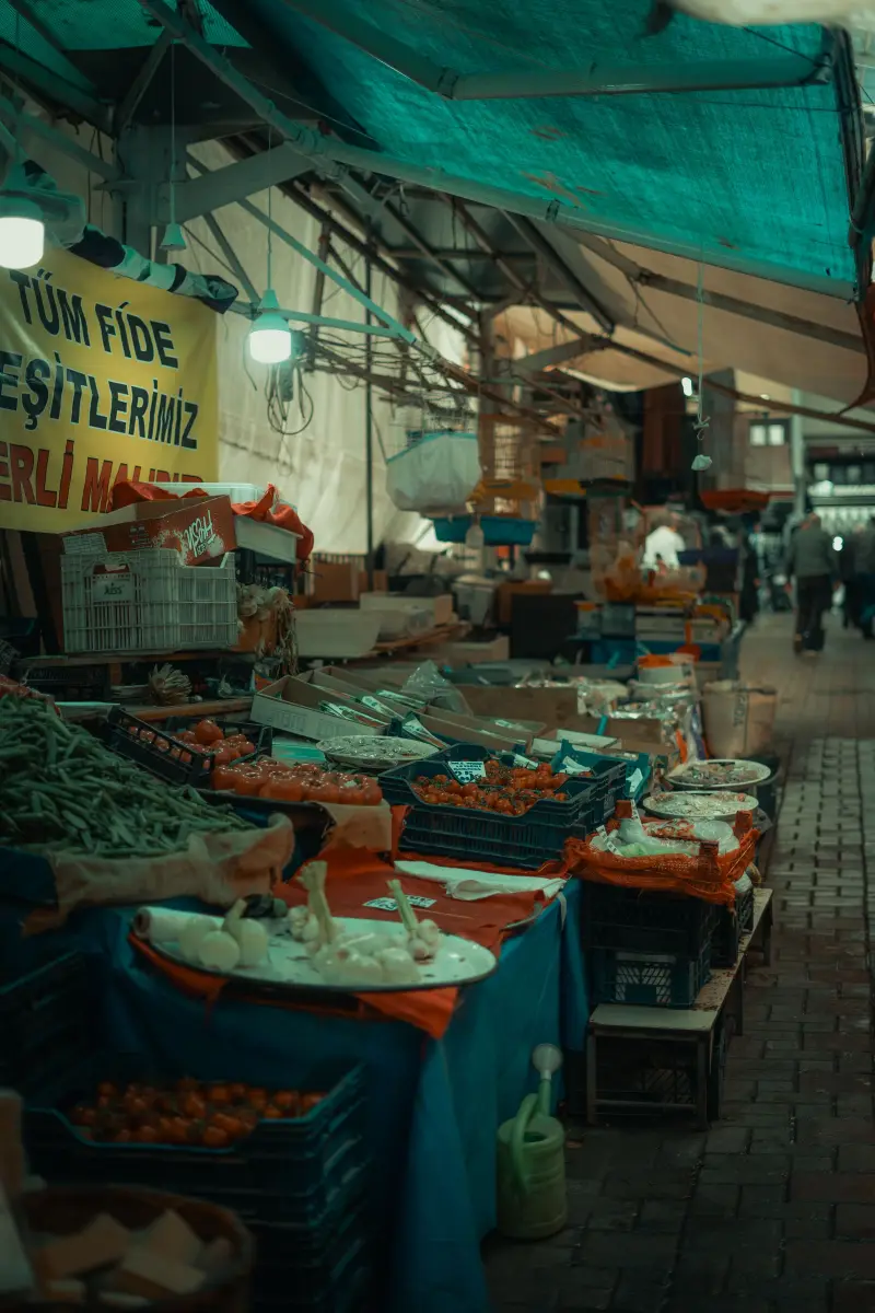 Mavi tenteli bir semt pazarında kasalarda domates, taze fasulye ve sarımsak dizili tezgâhlar