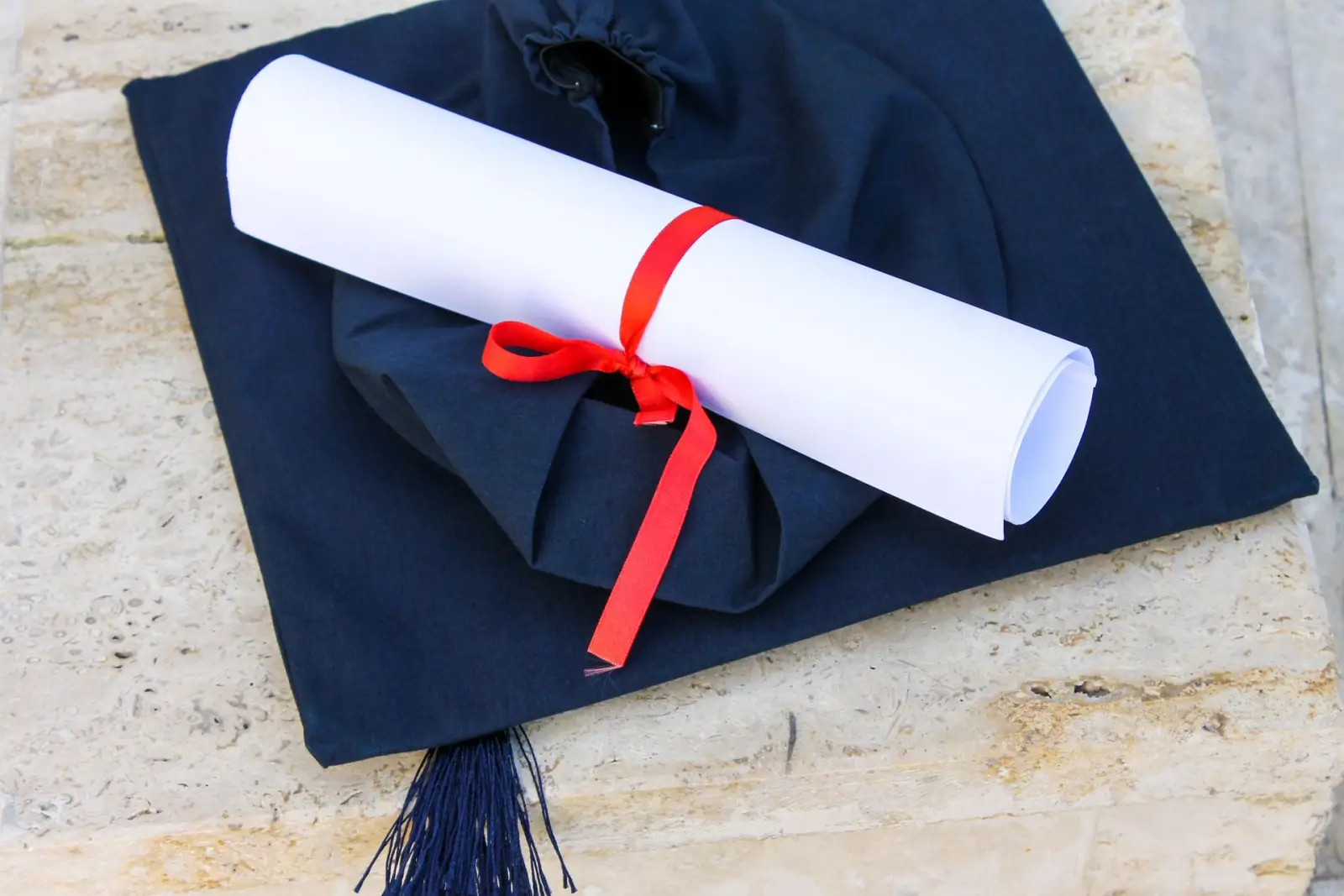 Taş zemin üzerinde lacivert kep ve kırmızı kurdeleyle bağlanmış diploma rulosu